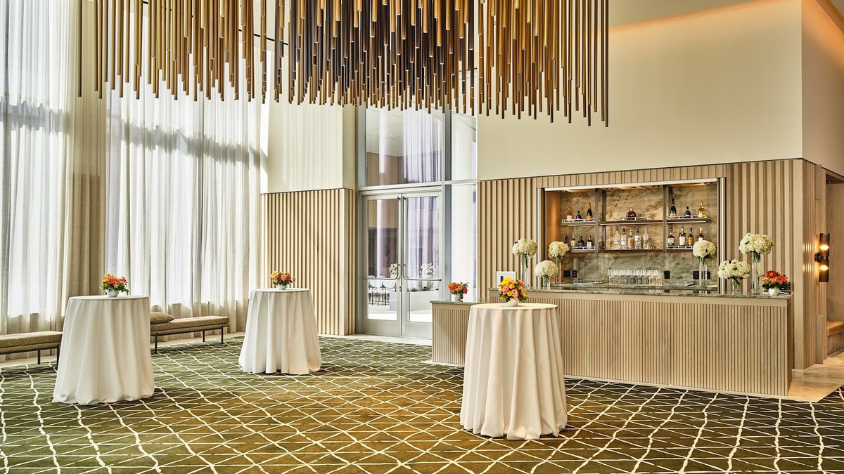 The Grand Park Foyer at Conrad Los Angeles with full-length windows, a marble bar and cocktail tables