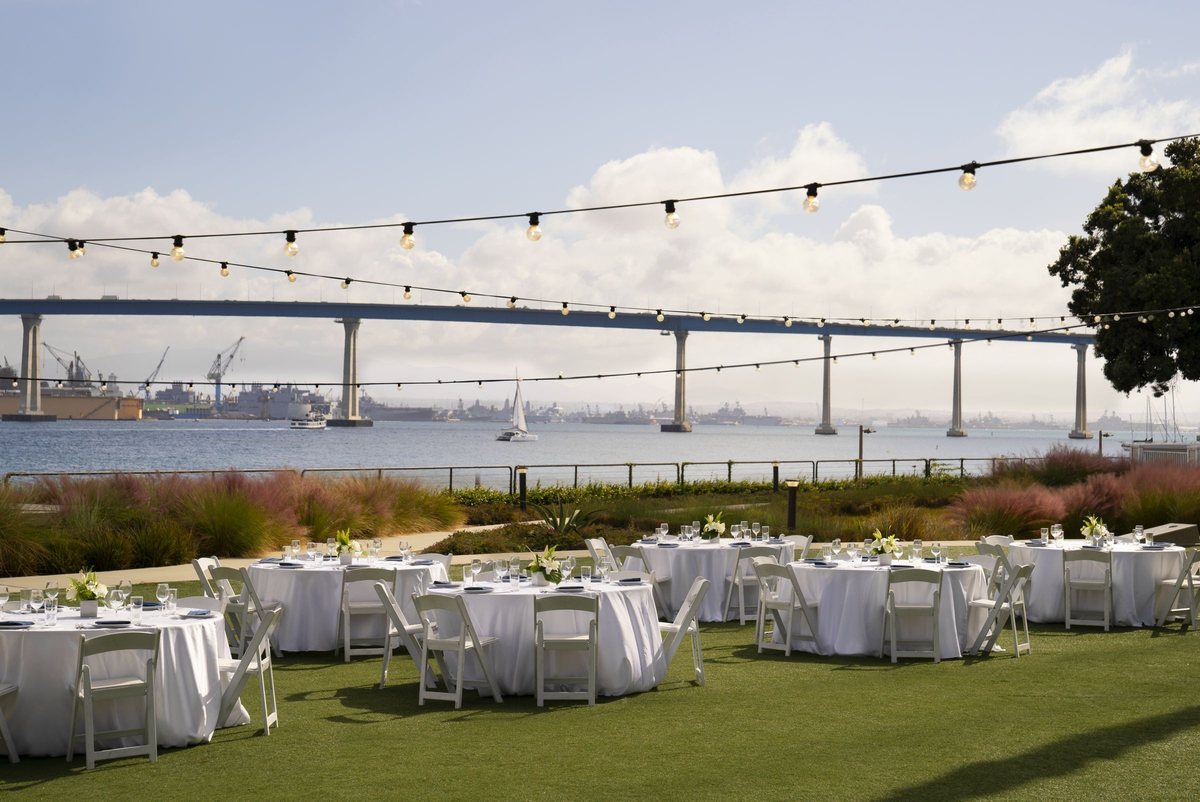 A daytime reception on a bayfront lawn at Coronado Island Marriott Resort & Spa, with string lights and the Coronado Bridge behind