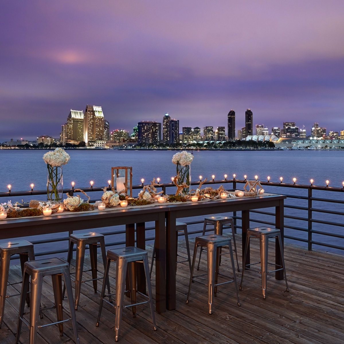 The Pier at Coronado Island Marriott Resort & Spa set with a long dinner table and the San Diego skyline at dusk