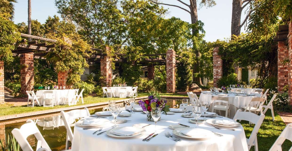 Round dinner tables in a garden setting beneath brick pillars and an arbor