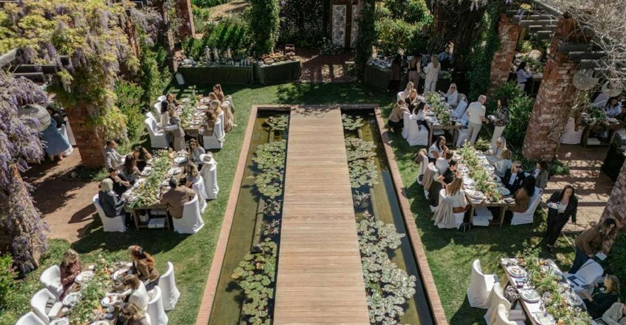 Long dinner tables set on either side of the lily pond under wisteria
