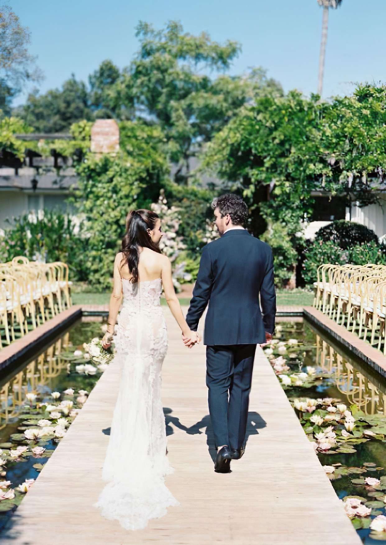 A wedding couple walking down the boardwalk over the lily pond