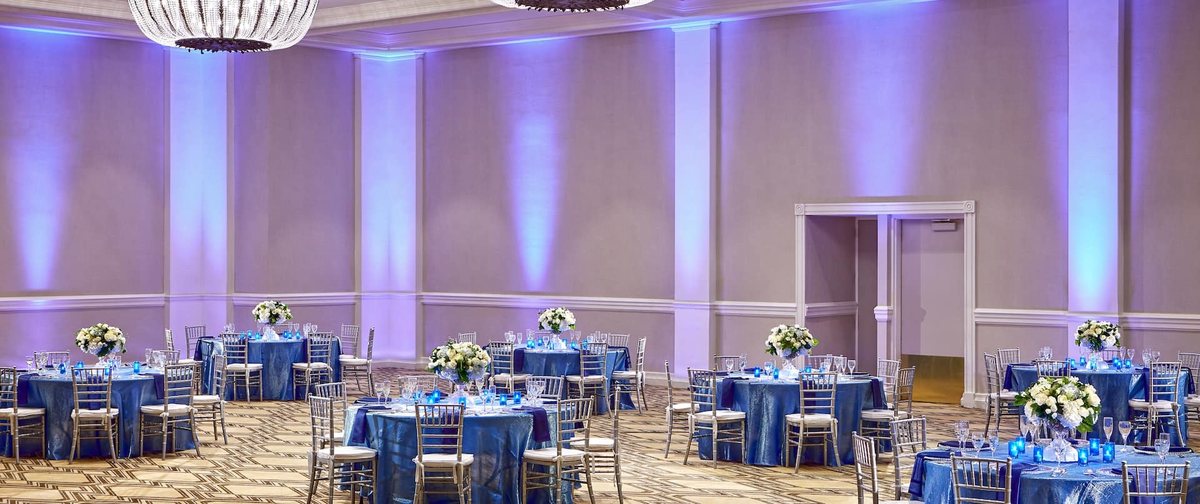 The International Ballroom at Hilton Pasadena set for a dinner with round tables, blue linens and lavender uplighting