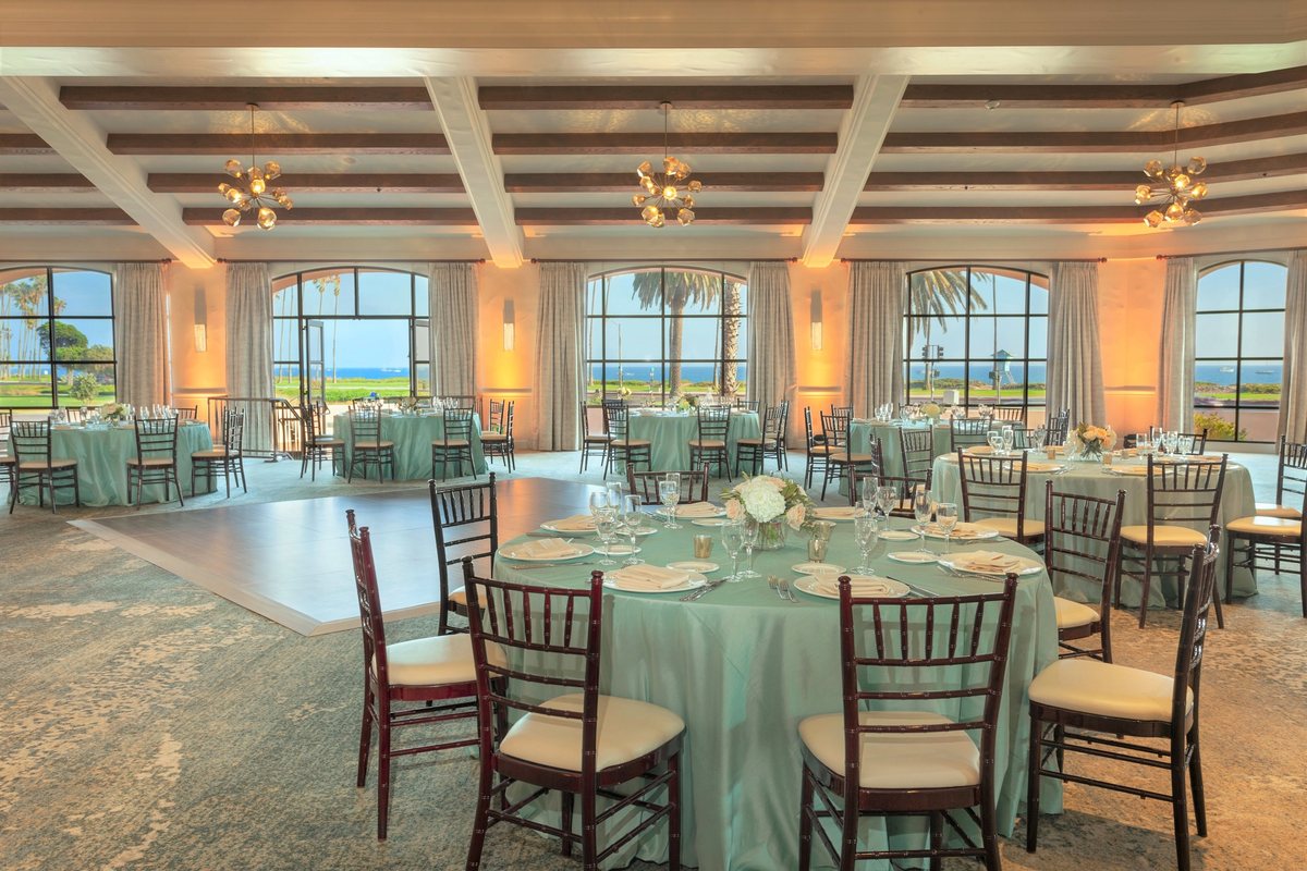 The Reagan Room at Hilton Santa Barbara Beachfront Resort set with round tables and chairs under a beamed ceiling