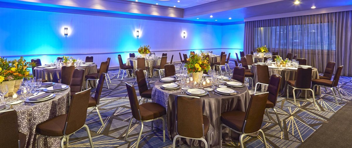 The Panache Ballroom at Hotel MdR set for a social event with round tables, flowers and blue uplighting