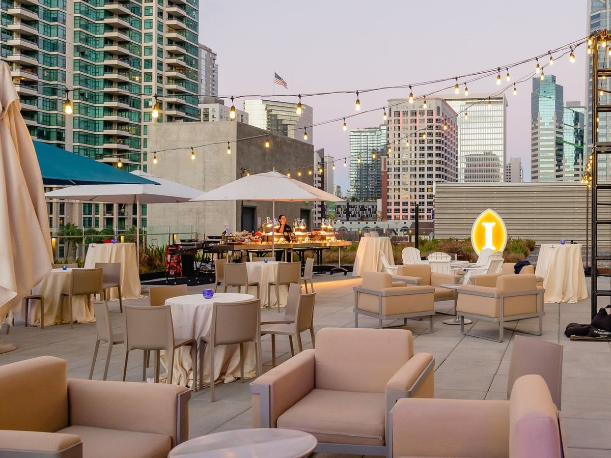 A rooftop terrace with lounge seating, string lights and the downtown San Diego skyline at dusk