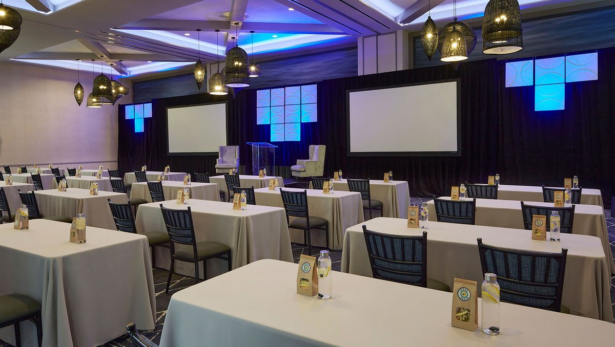 The Epic Ballroom at Kimpton Shorebreak set with tables facing two projection screens and colored uplighting