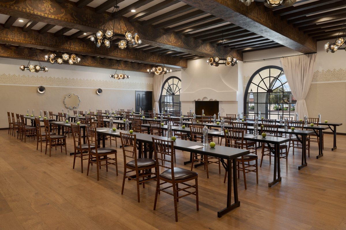 The Fireside ballroom at Mar Monte Hotel set classroom style under hand-painted beams with arched windows and a fireplace