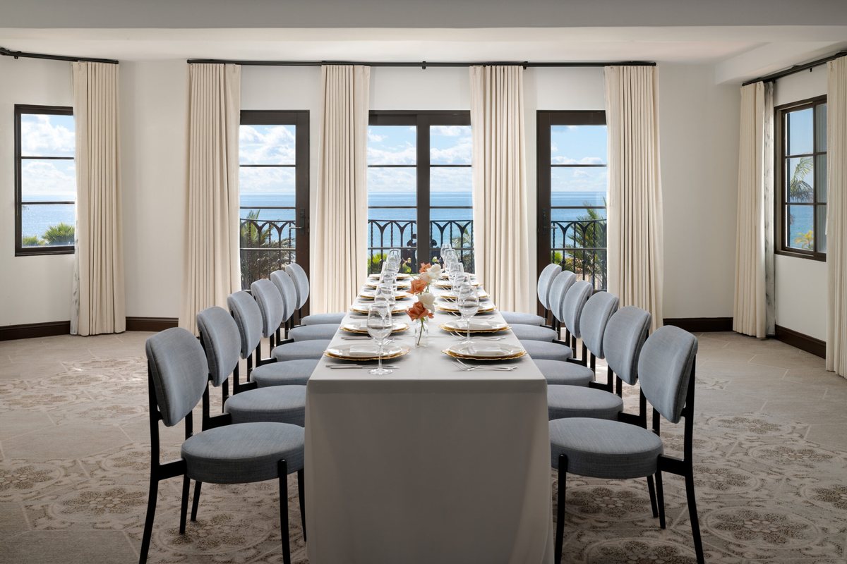 The Seaview room at Mar Monte Hotel set with a long dining table facing a Juliet balcony and ocean windows