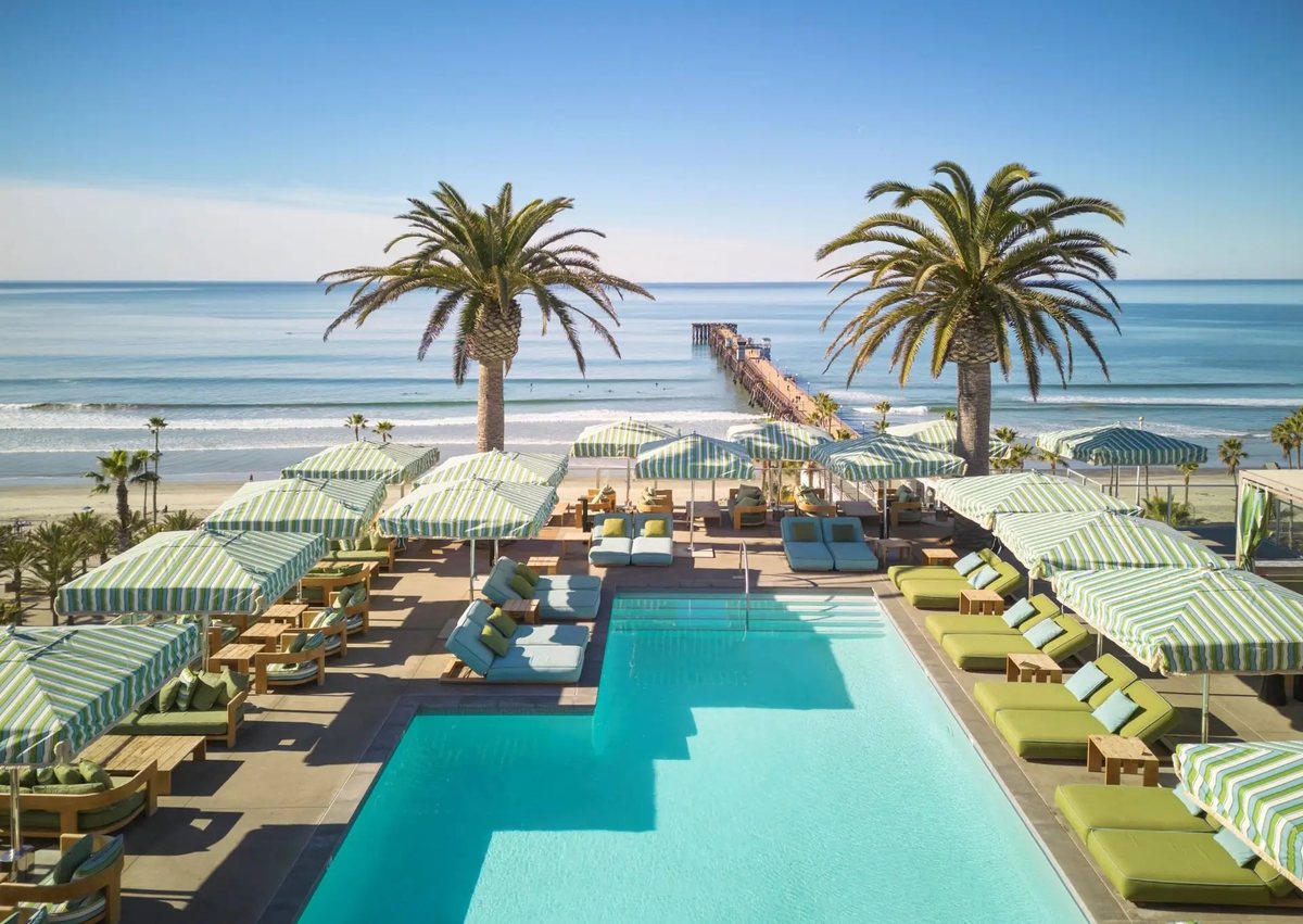 Aerial view of the rooftop pool deck at Mission Pacific Beach Resort with cabanas, palms and the ocean beyond