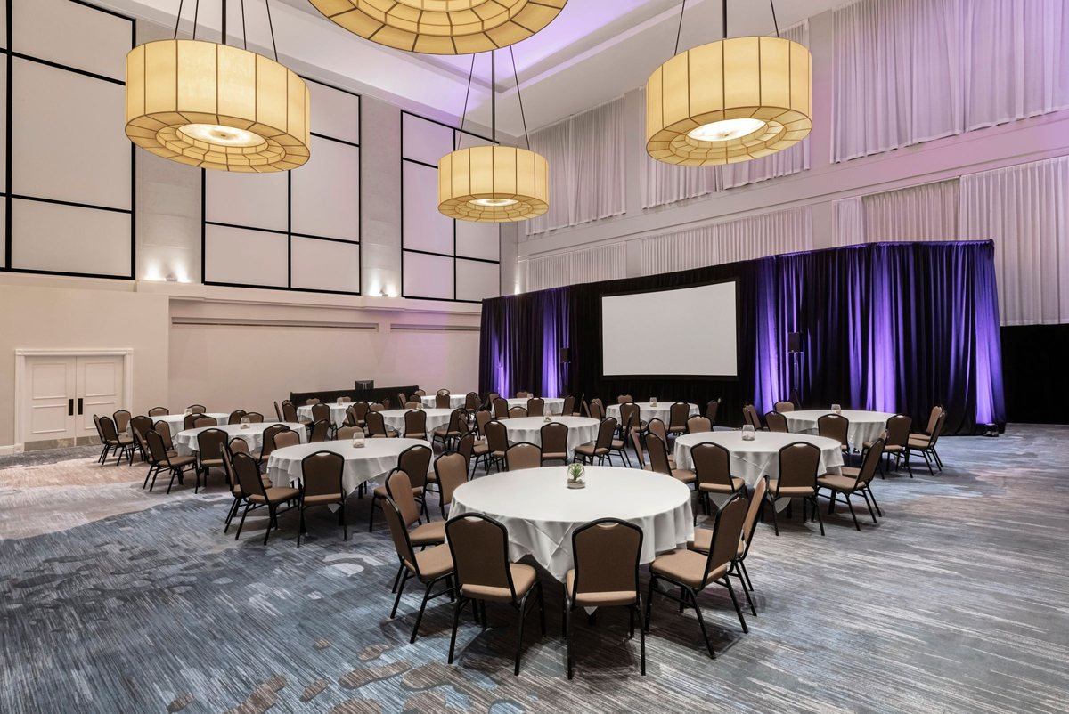 The Citrus Ballroom at Renaissance Newport Beach Hotel with round tables, large pendant lights and a stage with a screen