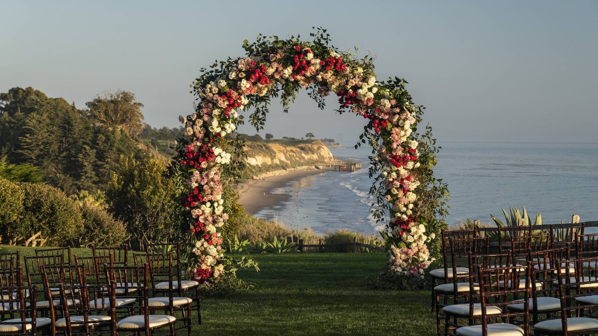 A floral ceremony arch with ocean and coastline views