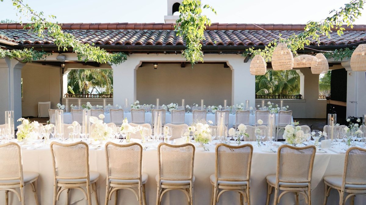 A long dinner table set beneath a tiled roof and greenery