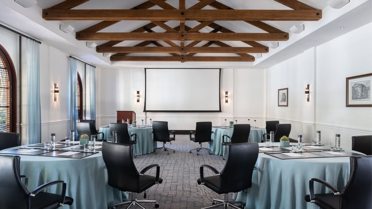 A salon with a beamed ceiling set with round tables and a projection screen
