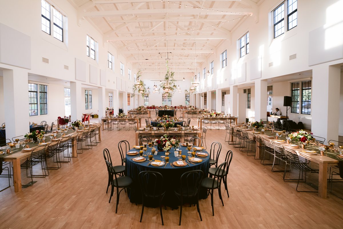 The Vesper Venue main hall set with long wooden banquet tables and a round head table under the vaulted ceiling