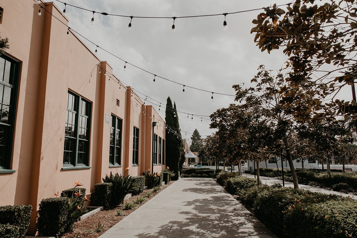 The outdoor patio along the side of the building with string lights overhead and a path between hedges
